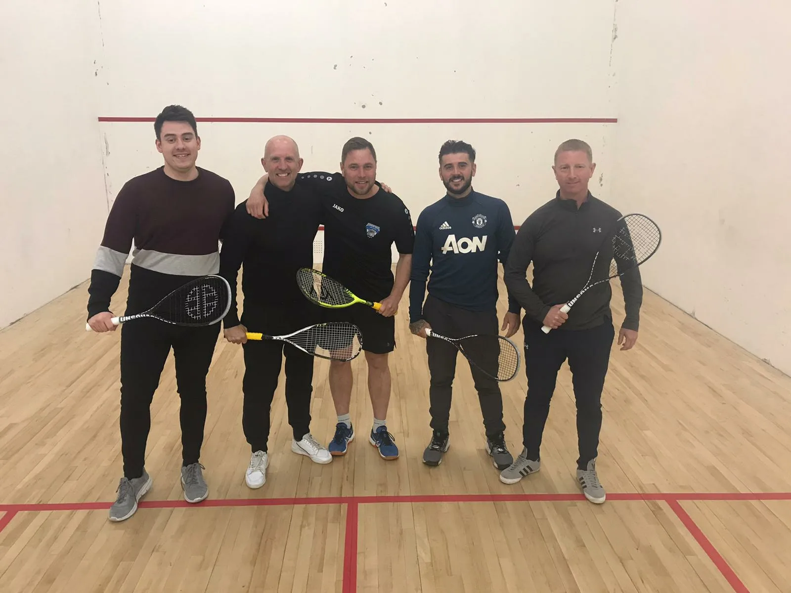 Five men in a squash court holding rackets